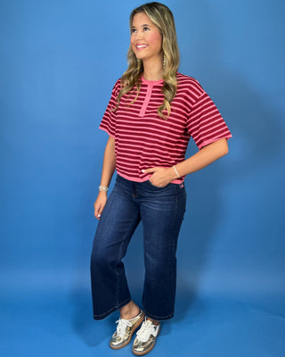Pink and burgundy striped short sleeve knit top with a round neckline, button placket, relaxed fit, and contrast pink trim.
