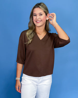 Woman wearing a brown shirt and white pants against a blue background