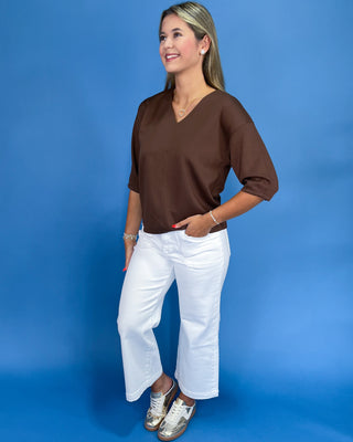 Woman wearing a brown top and white pants against a blue background