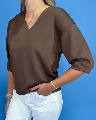 Person wearing a brown top and white pants against a blue background