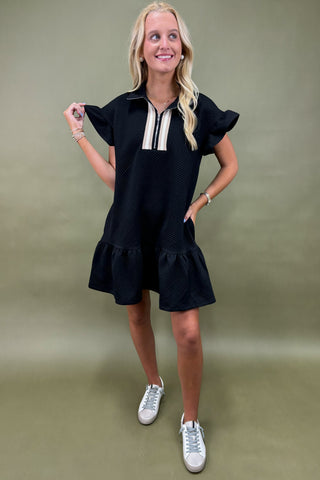 Woman wearing a black dress with white accents against a green background