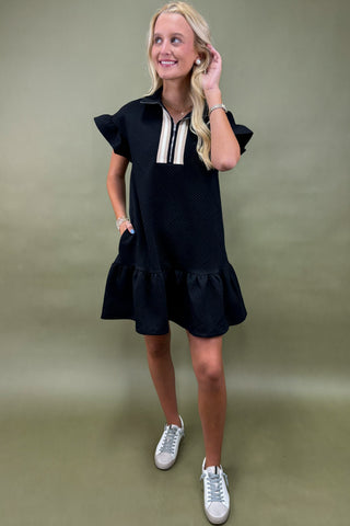 Woman wearing a black dress with white sneakers on a plain background