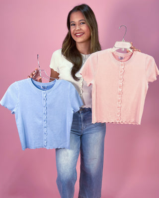 Woman holding two shirts, one blue and one pink, against a pink background