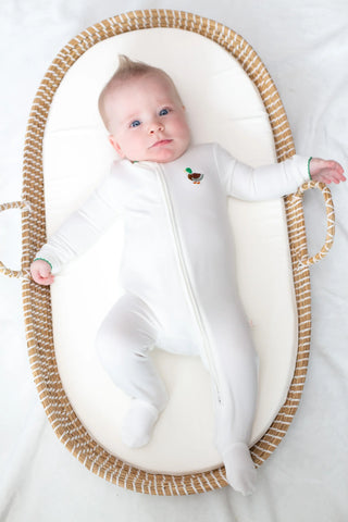 Baby in a white onesie with a small design lying in a woven basket on a white background