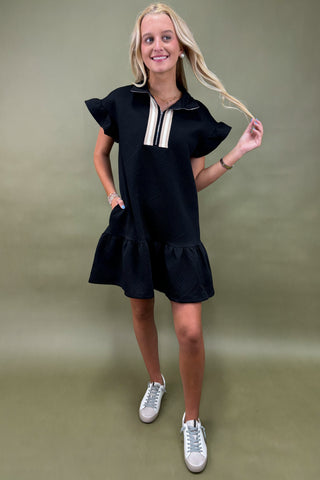 Woman wearing a black dress with ruffled sleeves and bottom hem against a green background