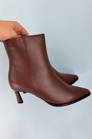 Brown leather ankle boots with a slight heel on a light blue background