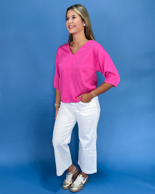 Woman wearing a bright pink top and white pants against a blue background