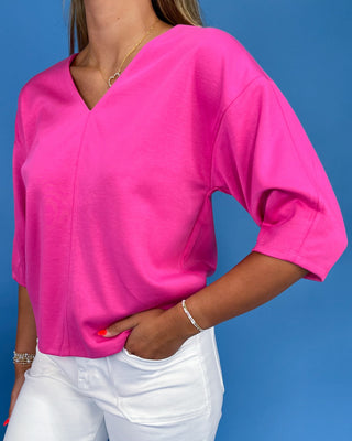 Person wearing a bright pink top and white pants against a blue background