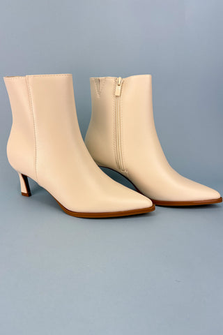 Pair of beige ankle boots with brown soles on a gray background