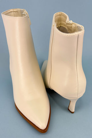 Pair of beige ankle boots with brown soles on a blue background