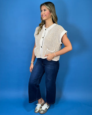 Cream and taupe chunky knit sweater vest with a button-front design, cap sleeves, contrast vertical stitching, and front patch pockets.