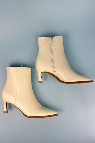Pair of beige ankle boots with brown soles on a light blue background