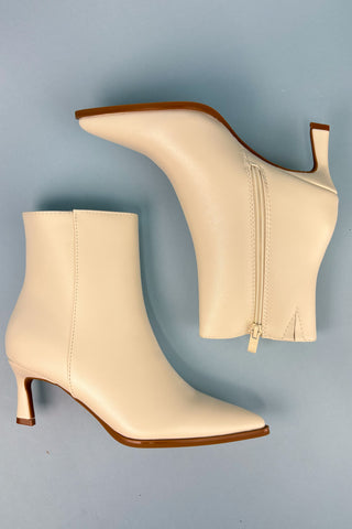 Pair of beige ankle boots with brown soles on a light blue background