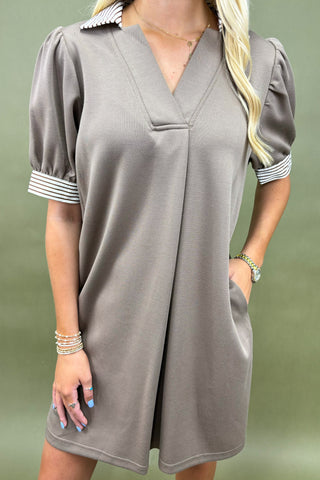 Woman wearing a gray dress with short sleeves and striped cuffs against a green background