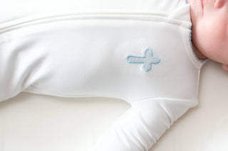 Close-up of a baby's arm in a white sleeve with a blue flower design on a white background