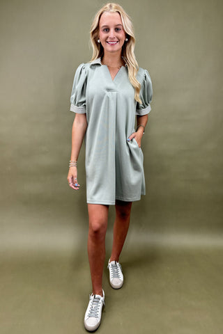 Woman wearing a light green dress with puff sleeves against a plain background
