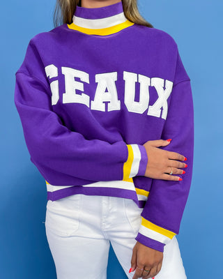 Purple sweater with 'JEAUX' text worn by a person against a blue background