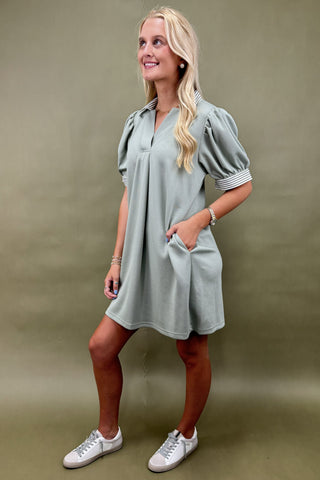Woman wearing a light gray dress with puff sleeves against a green background