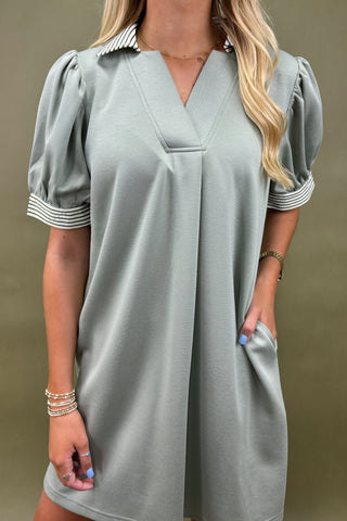 Woman wearing a gray dress with short sleeves and striped cuffs against a brown background