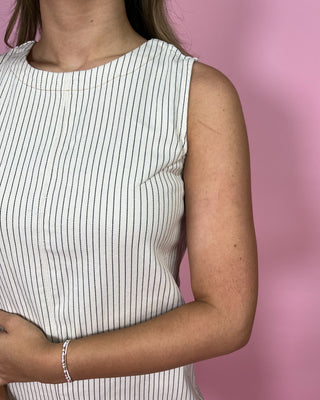 Person wearing a white sleeveless top with black stripes against a pink background