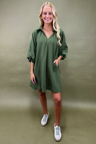 Woman wearing a green dress with white sneakers against a plain background