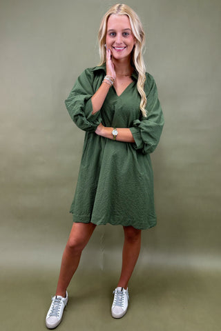 Woman wearing a green dress with long sleeves against a plain background