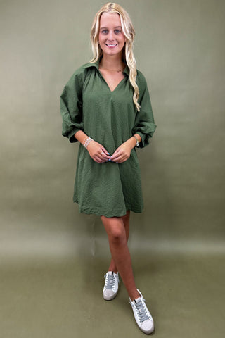 Woman wearing a green dress with white sneakers against a green background