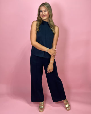 Woman wearing a navy sleeveless top and wide-leg pants against a pink background
