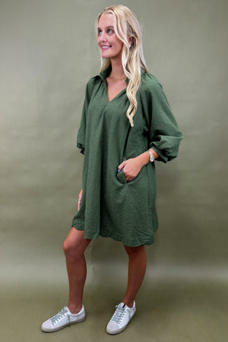 Woman wearing a green dress with white sneakers on a beige background