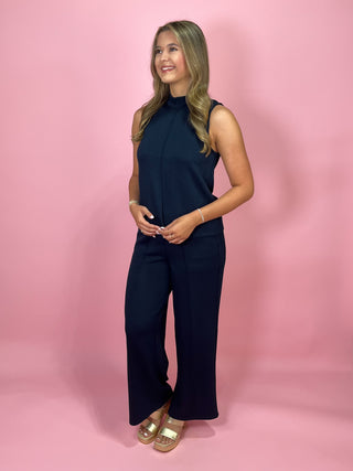 Woman wearing a navy blue sleeveless jumpsuit on a pink background