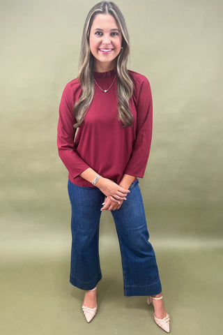 Woman wearing a red top and blue jeans against a green background