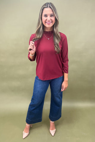 Woman wearing a red top and blue jeans against a green background