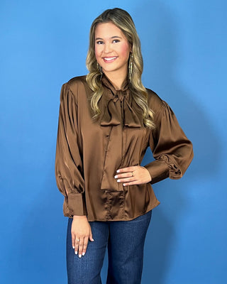 Chocolate brown satin blouse with a statement tie-neck bow, long balloon sleeves, button cuffs, and an elegant relaxed silhouette.