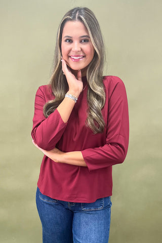 Woman wearing a burgundy top and blue jeans against a beige background