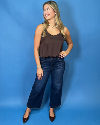 A woman modeling a sleeveless brown top and dark blue wide-leg jean