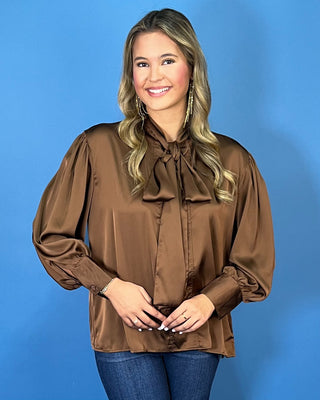 Chocolate brown satin blouse with a statement tie-neck bow, long balloon sleeves, button cuffs, and an elegant relaxed silhouette.