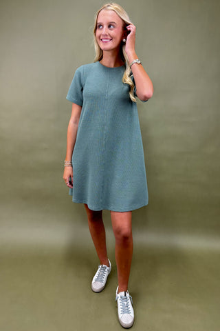 Woman wearing a teal dress and white sneakers against a plain background