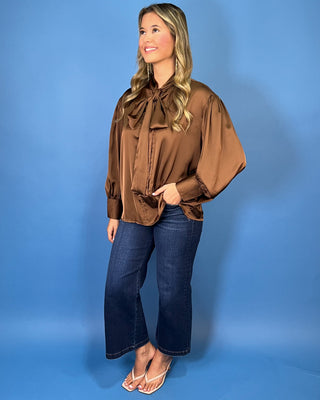 Chocolate brown satin blouse with a statement tie-neck bow, long balloon sleeves, button cuffs, and an elegant relaxed silhouette.
