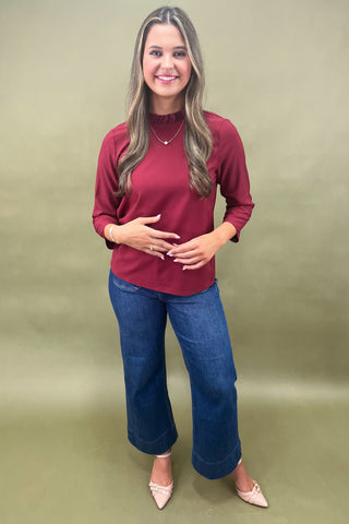 Woman wearing a red top and blue jeans against a green background