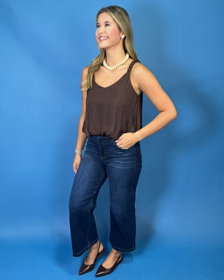 A woman modeling a brown sleeveless top and dark blue wide-leg jeans
