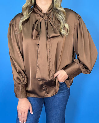 Chocolate brown satin blouse with a statement tie-neck bow, long balloon sleeves, button cuffs, and an elegant relaxed silhouette.