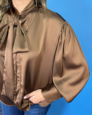 Chocolate brown satin blouse with a statement tie-neck bow, long balloon sleeves, button cuffs, and an elegant relaxed silhouette.