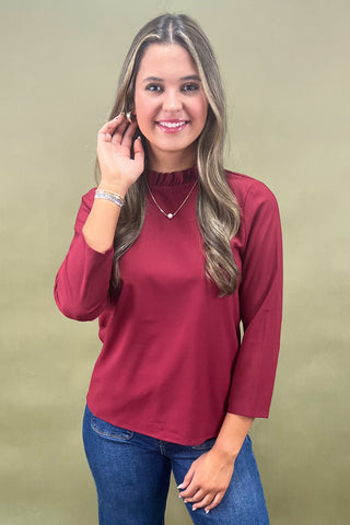 Woman wearing a burgundy top and blue jeans against a beige background