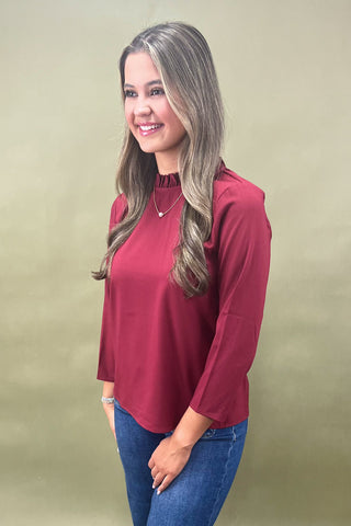 Woman wearing a red blouse and blue jeans against a beige background