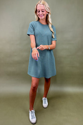Woman wearing a teal dress with white sneakers on a plain background