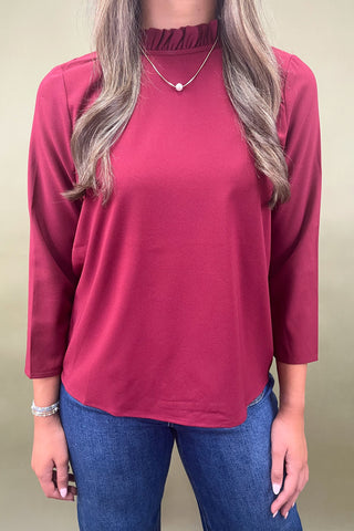 Person wearing a maroon long-sleeve top and blue jeans against a beige background