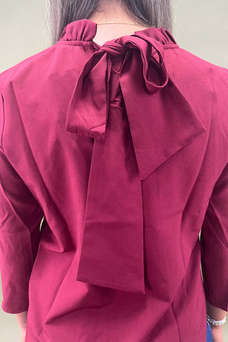 Close-up of a red blouse with a large bow at the neckline.