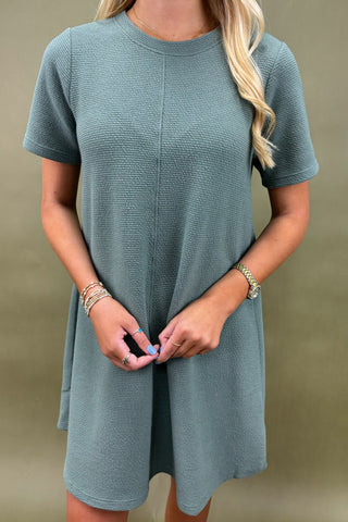 Woman wearing a teal dress against a beige background