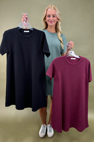 Woman holding a black dress on one hanger and a maroon dress on another against a plain background
