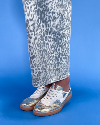 Silver sneakers with white laces worn with leopard print pants on a blue background